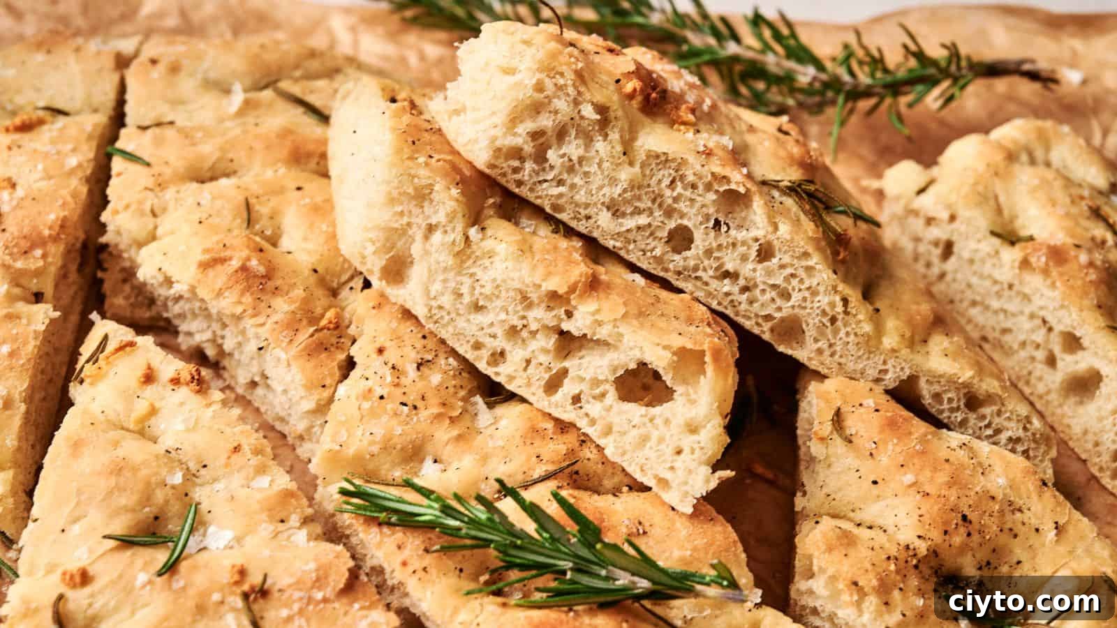 Slices of focaccia bread topped with rosemary and flaky salt, arranged on brown parchment paper.