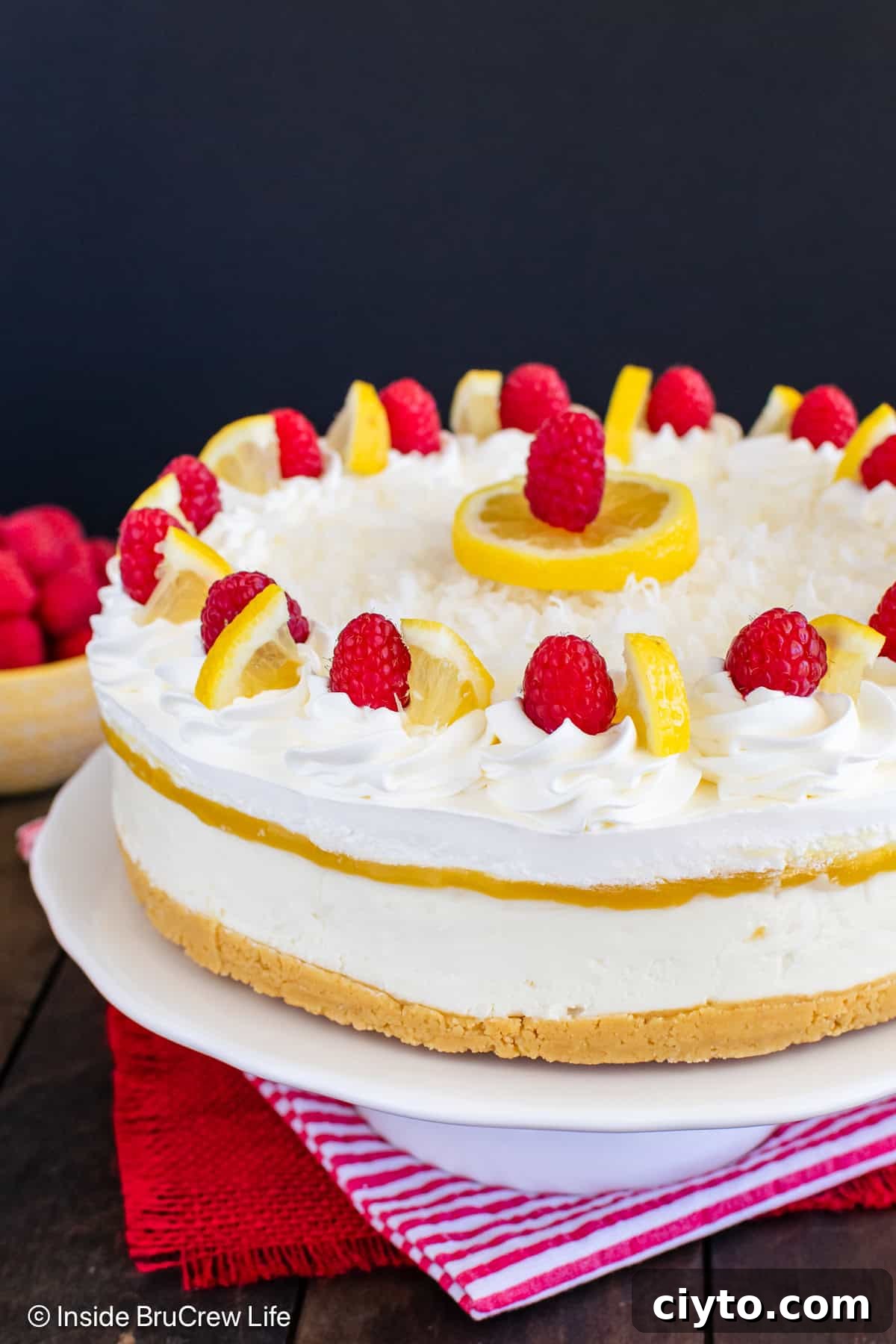 No-Bake Lemon Coconut Cheesecake Recipe 6 A close up of the side of a lemon coconut cheesecake topped with Cool Whip and raspberries.