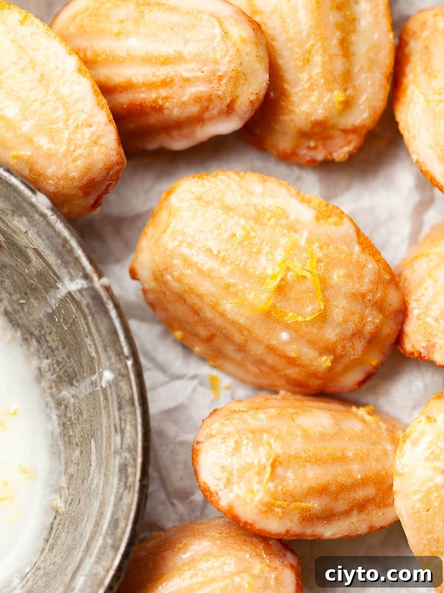 gluten free lemon madeleines topped with a quick lemon glaze and some fresh lemon zest next to a silver bowl 