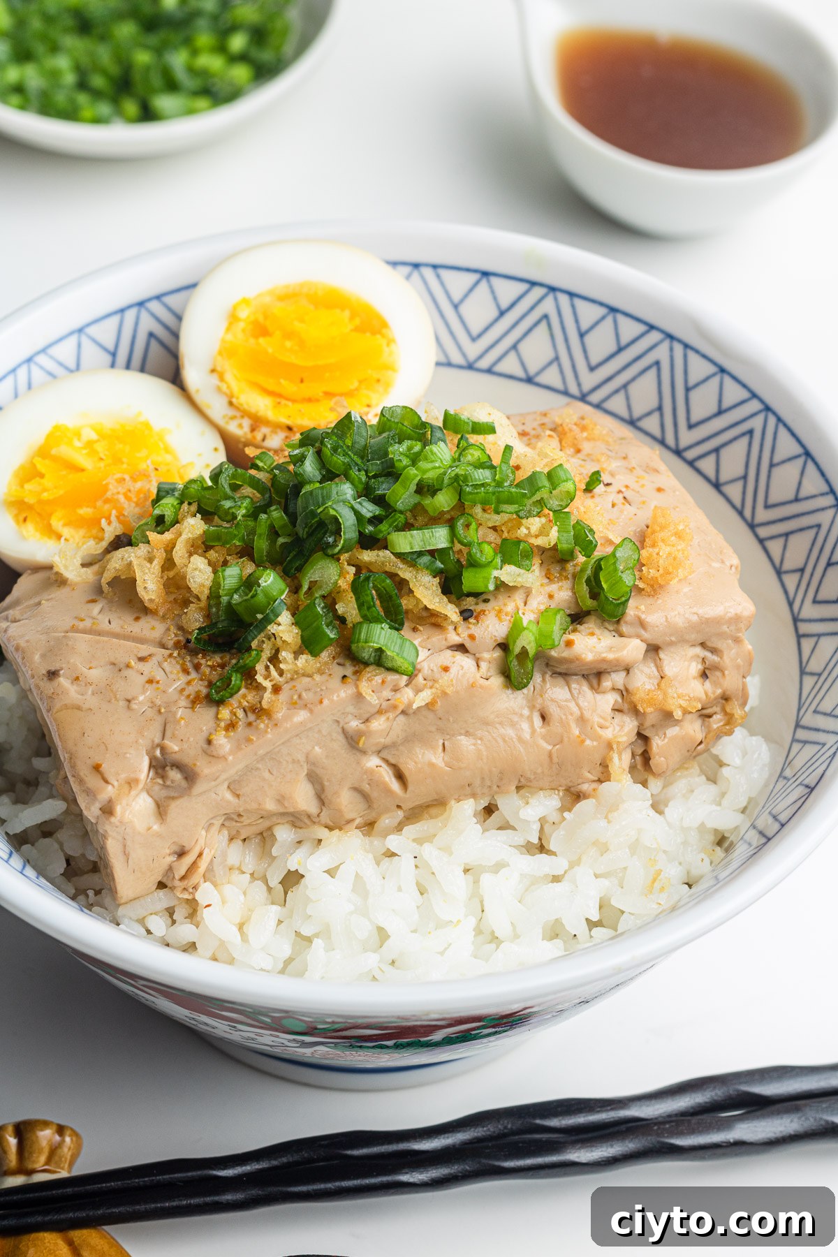 tofu and eggs over rice in a donburi bowl with scallions and tempura scraps on top