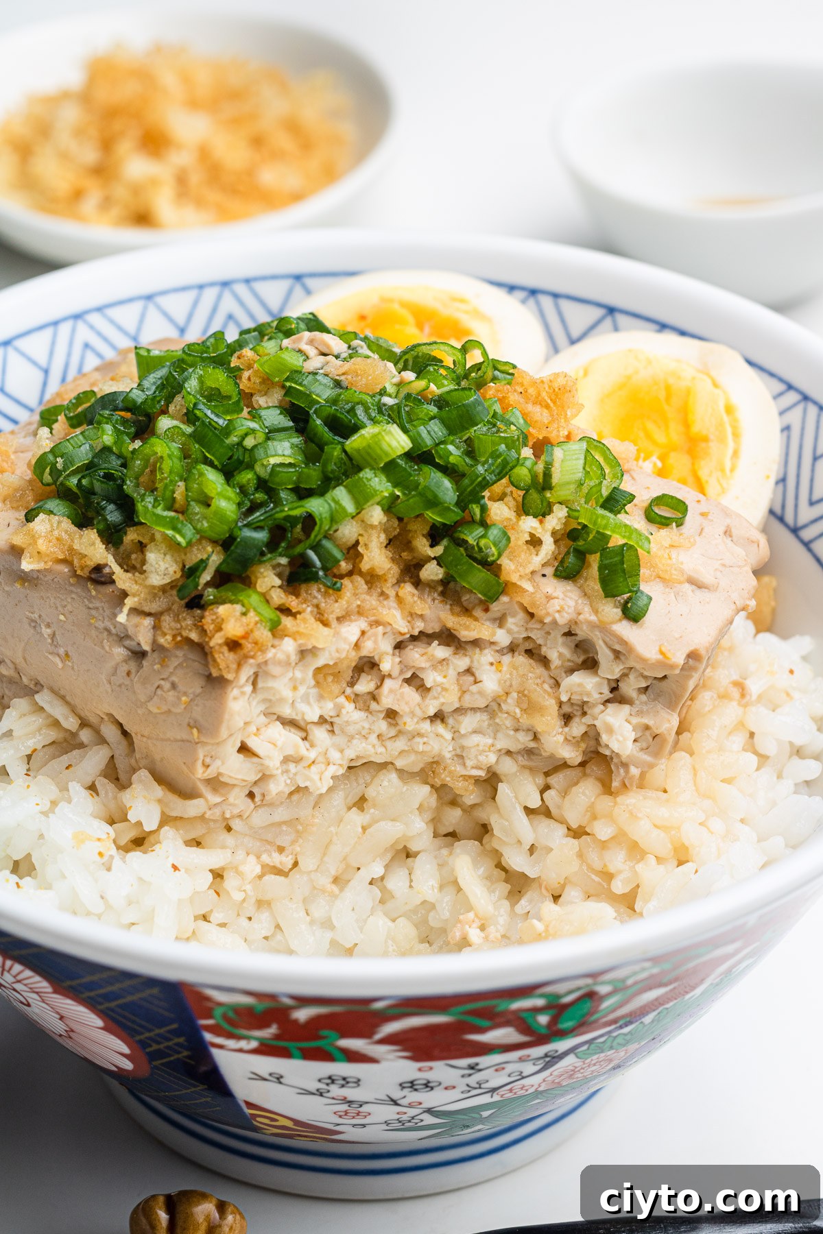 tofu and eggs (toumeshi) over rice in a donburi bowl with scallions and tempura scraps on top