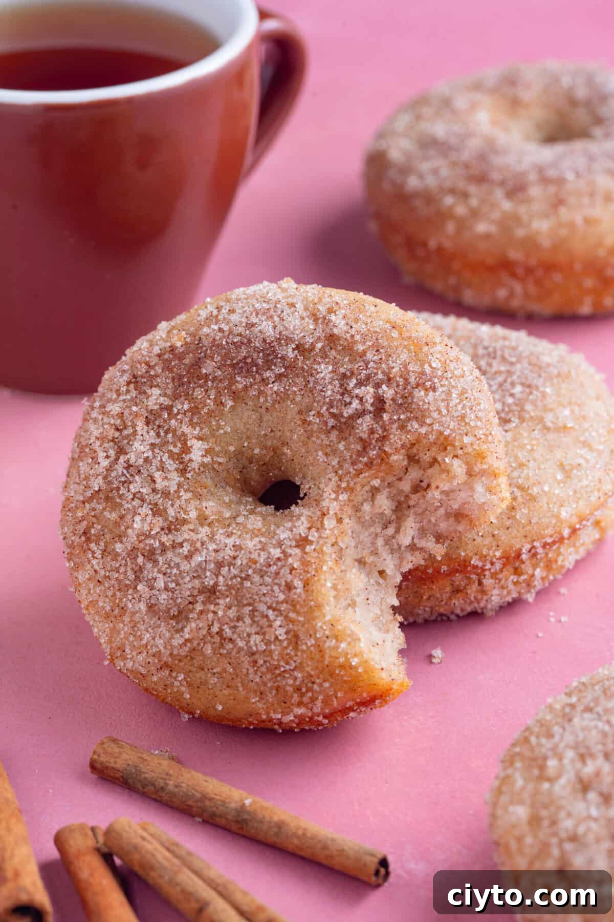 A gluten free doughnut with a bite taken out of it and a cup of tea in the backgound.