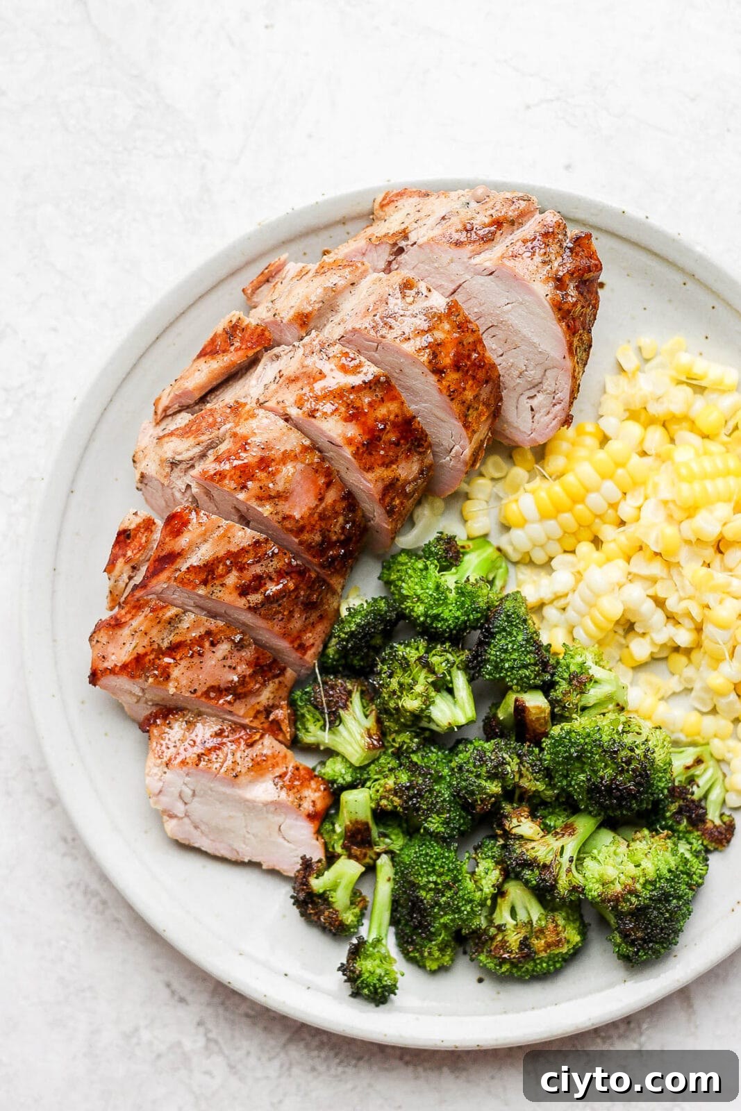 Smoked broccoli on a plate with sliced pork tenderloin and corn.