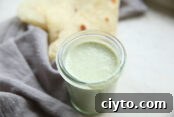 A jar of cilantro ranch dressing next to a grey napkin with a folded flour tortilla sitting on top of the napkin.