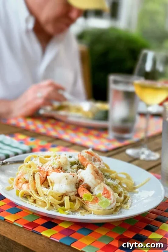 A white plate filled with shrimp and leek pasta on a multi-colored woven placemat.