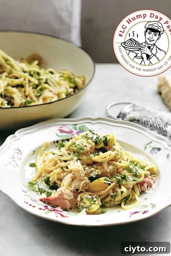Floral pasta bowl, filled with crab pasta, sprinkled with parsley and Parmesan. A cheese grater and larger bowl in the background.