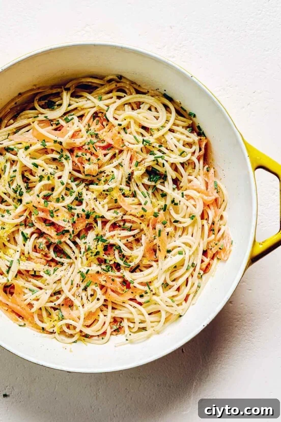 A yellow and white pot filled with smoked salmon pasta and garnished with fresh chives.