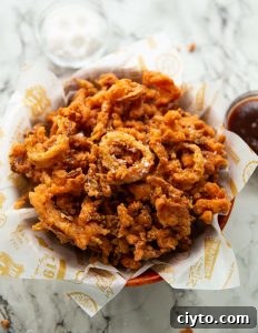 Crispy Fried Onions fried onions in wooden bowl with salt and bbq sauce blurred in background
