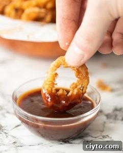 Crispy Fried Onions close up shot of hand dunking in crispy onion to small glass pot of bbq sauce