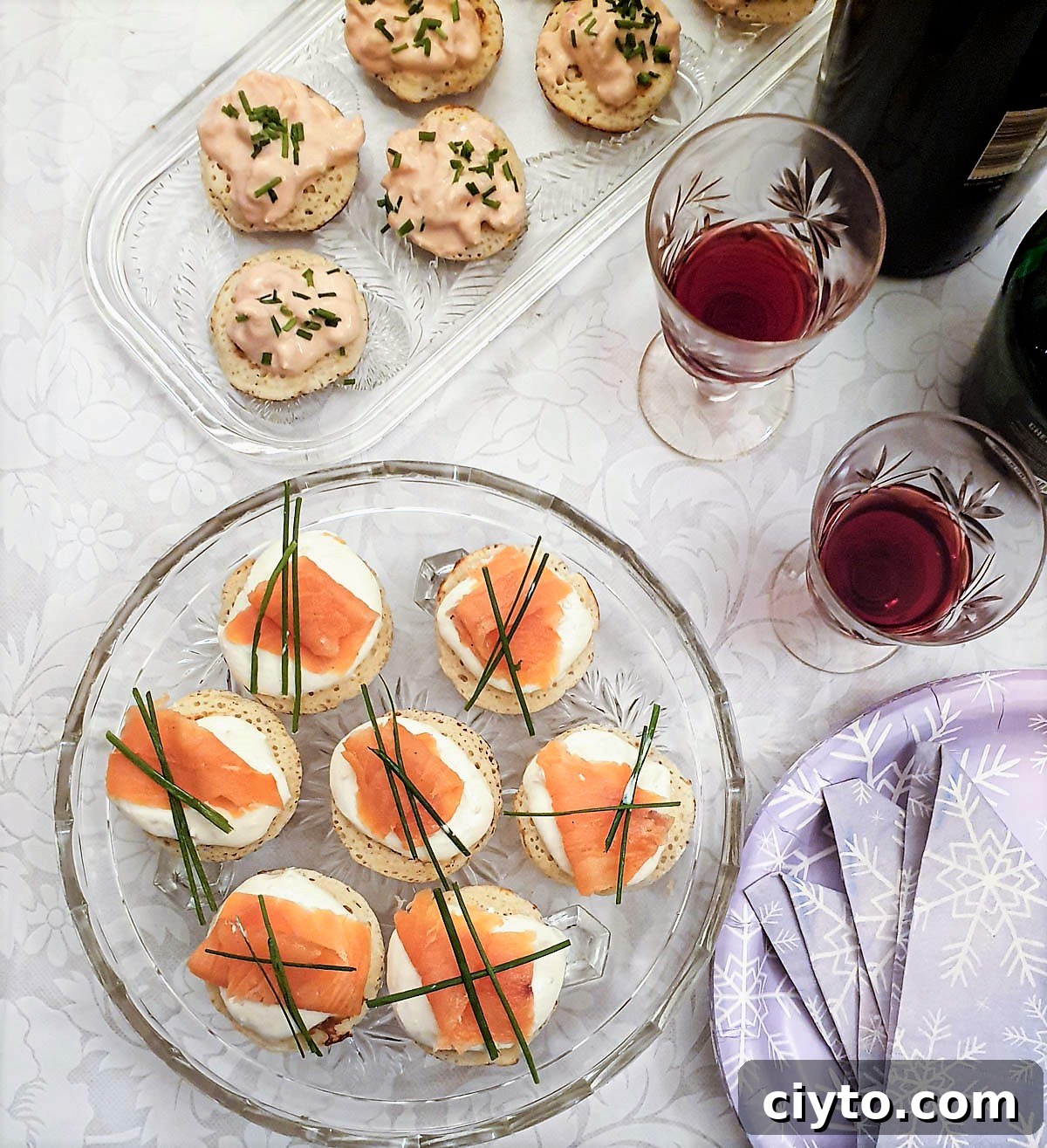 A selection of blinis on glass platters next to glasses of wine.