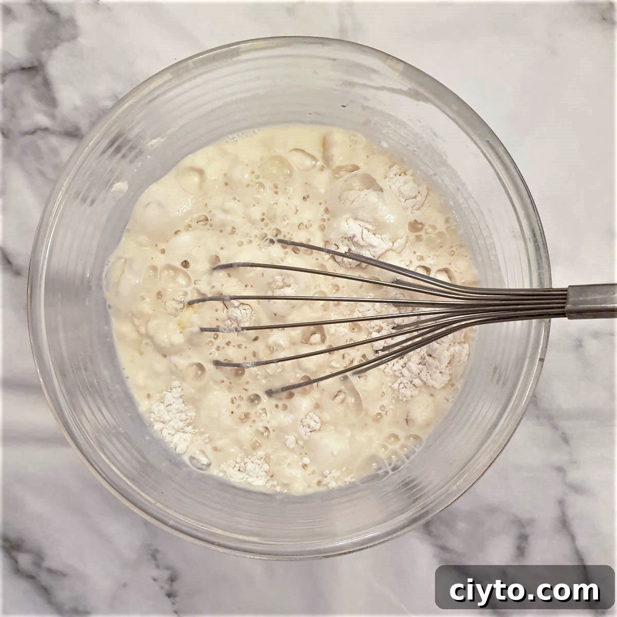 Blini batter being mixed in a bowl with a balloon whisk.
