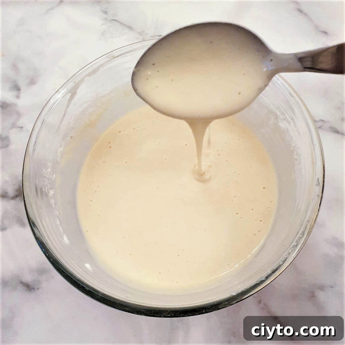 Blini batter being dropped from a spoon to show the consistency.