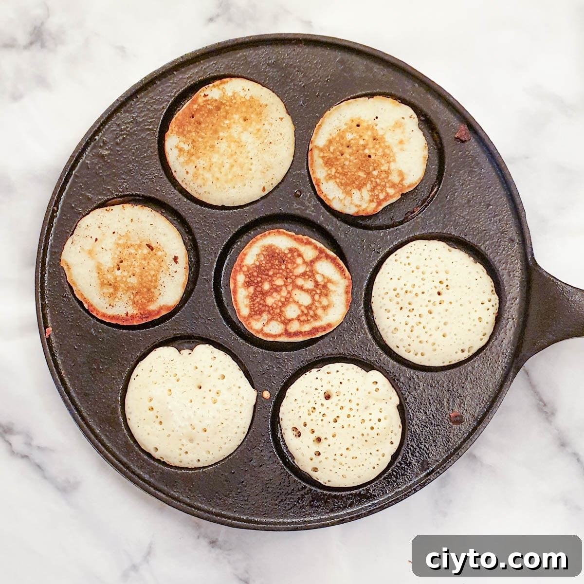 Blinis being browned in a blini pan.