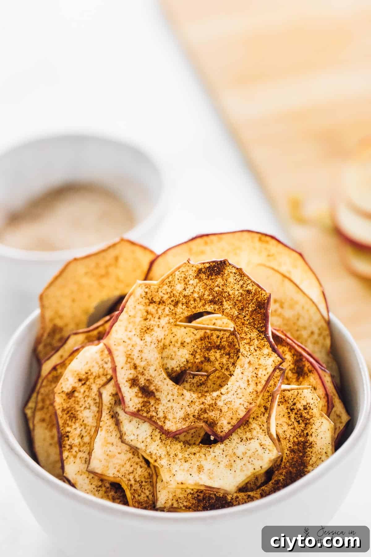 Easy homemade apple chips are crispy, chewy, rich, sweet, and covered in spicy cinnamon, making them the perfect fall snack. Close up of a bowl of apple chips covered in cinnamon sugar.