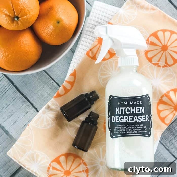 orange and lemon essential oil bottles on orange towel next to homemade kitchen degreaser spray bottle