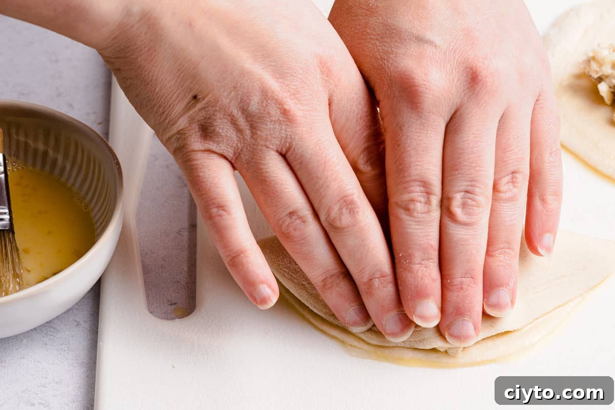 hands pressing edges of biscuit dough together to enclose turnover