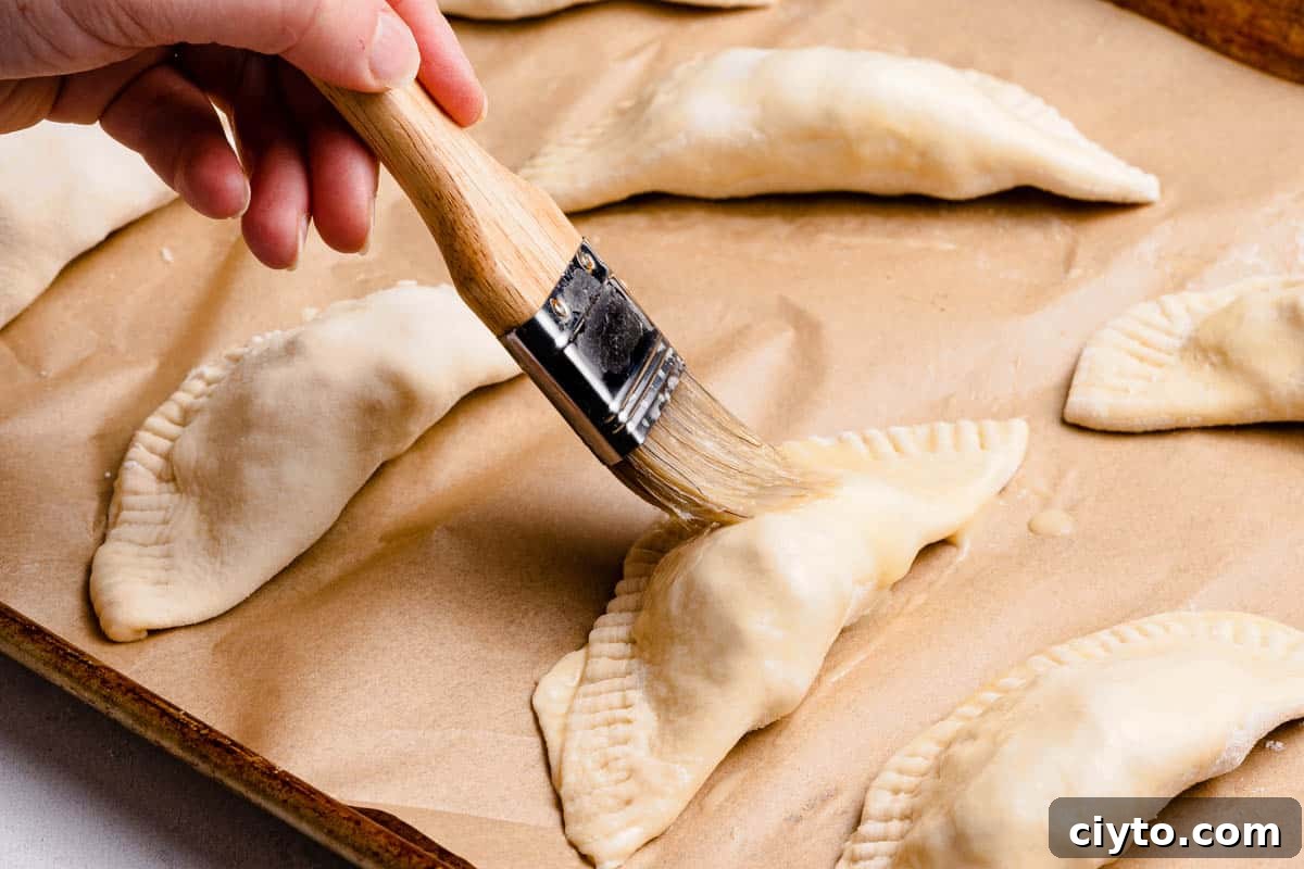 pastry brush brushing egg wash on top of unbaked turnover