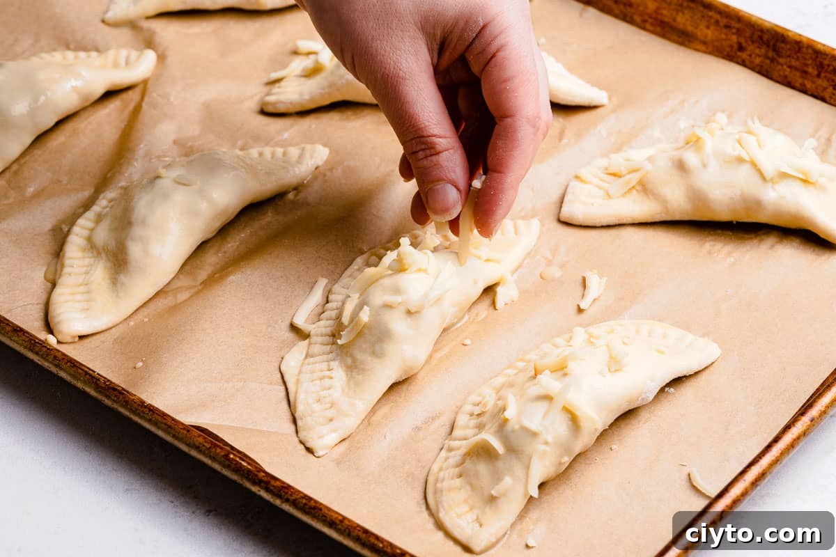 shredded cheese being sprinkled overtop unbaked turnovers