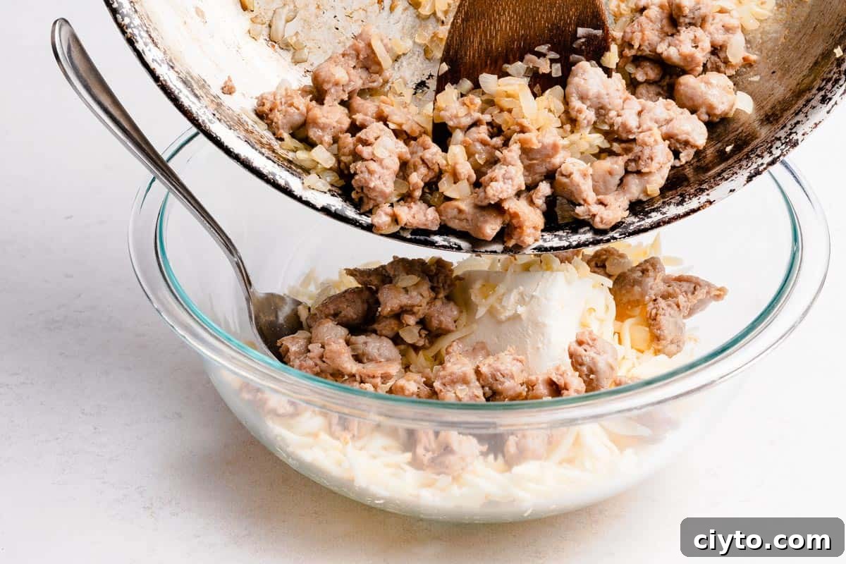 cooked sausage and onions being poured into bowl with cream cheese and shredded cheese inside