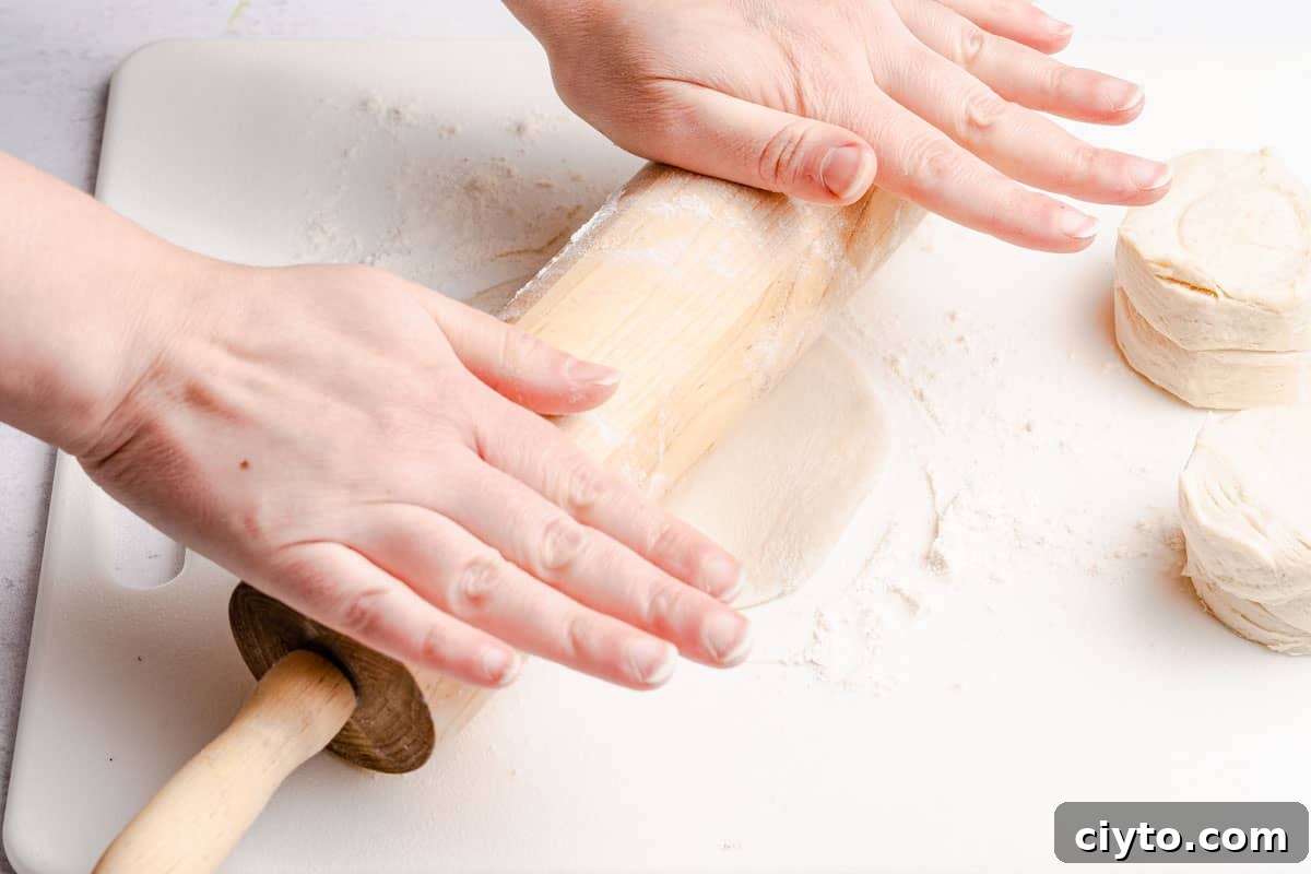 wooden rolling pin rolling out biscuit dough on cutting board