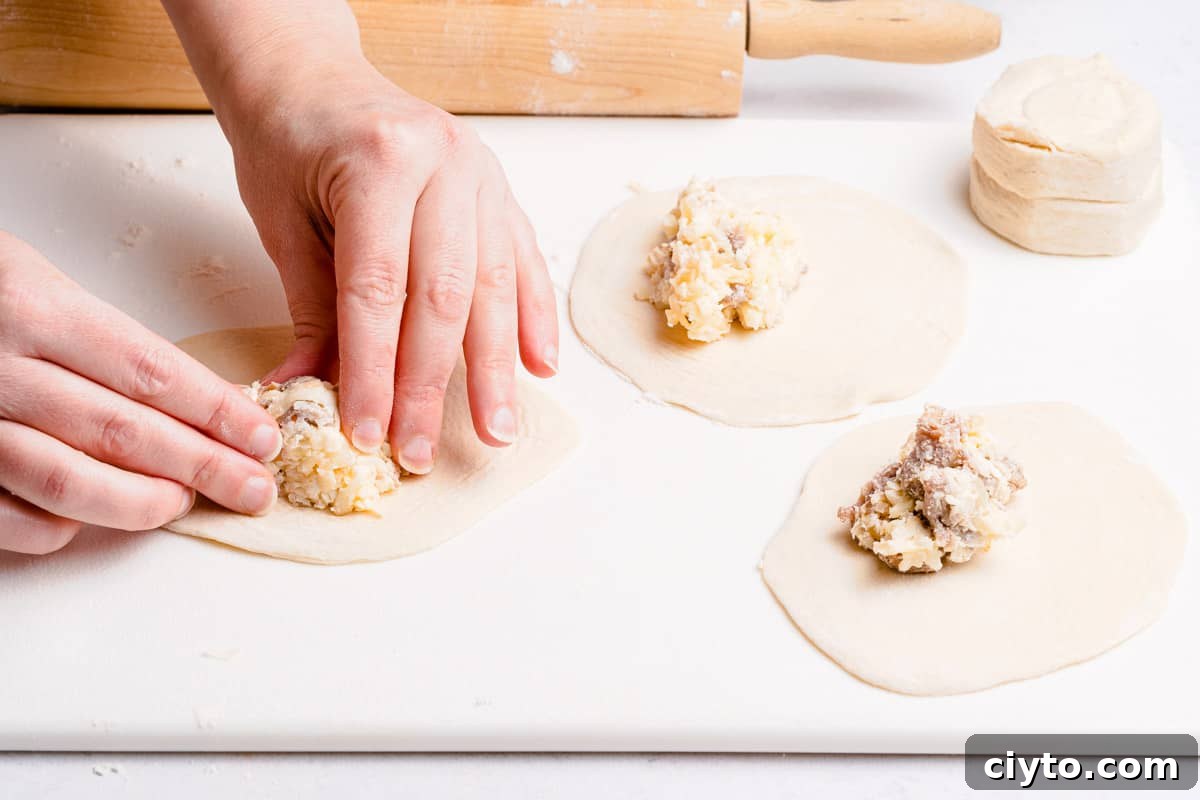 hands pressing mound of sausage and cheese filling to center of biscuit dough
