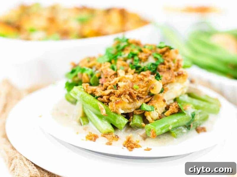 A serving of green bean casserole topped with crispy fried onions and chopped herbs, plated on a white dish.
