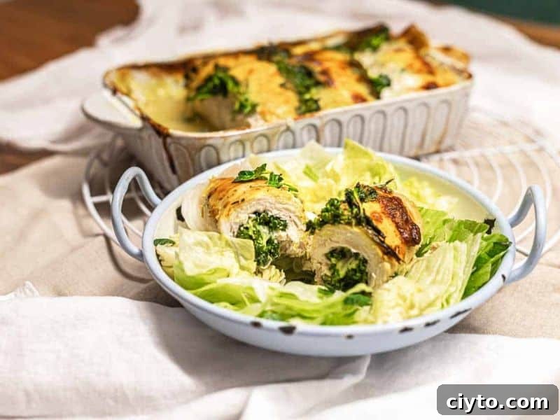 A white dish with rolled chicken stuffed with greens is baked and sliced, served on a bed of lettuce in a separate bowl.