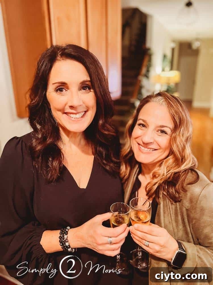 two woman standing in home toasting champagne in glasses smiling at camera