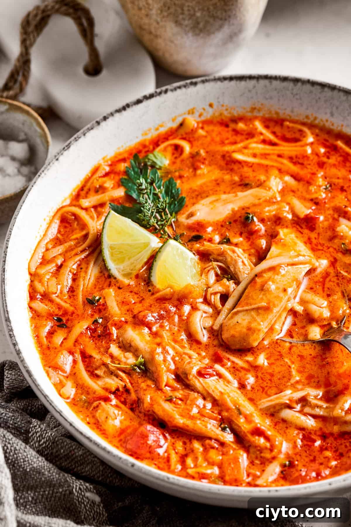 Close-up image of spicy chicken soup served in a bowl and garnished with lime wedges.