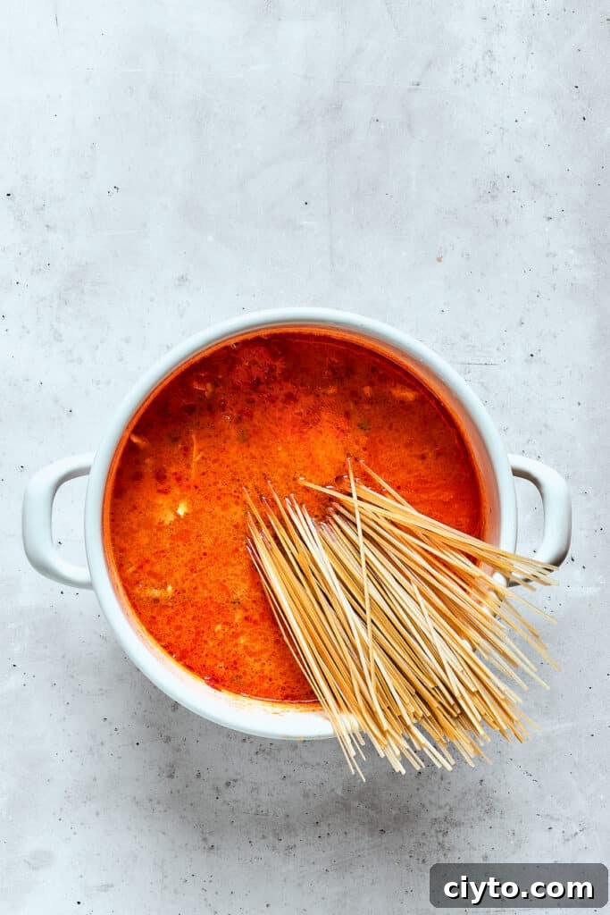 Rice noodles are added to a pot of spicy chicken soup.