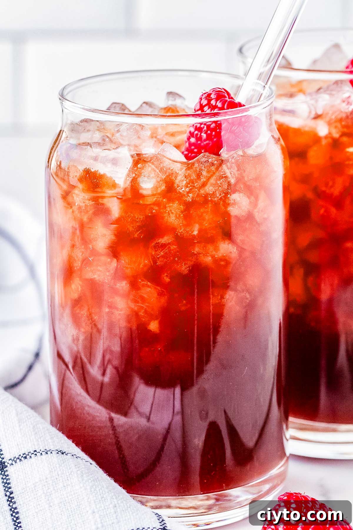 A Raspberry Dream drink in a clear glass with pebble ice and a raspberry for garnish. 
