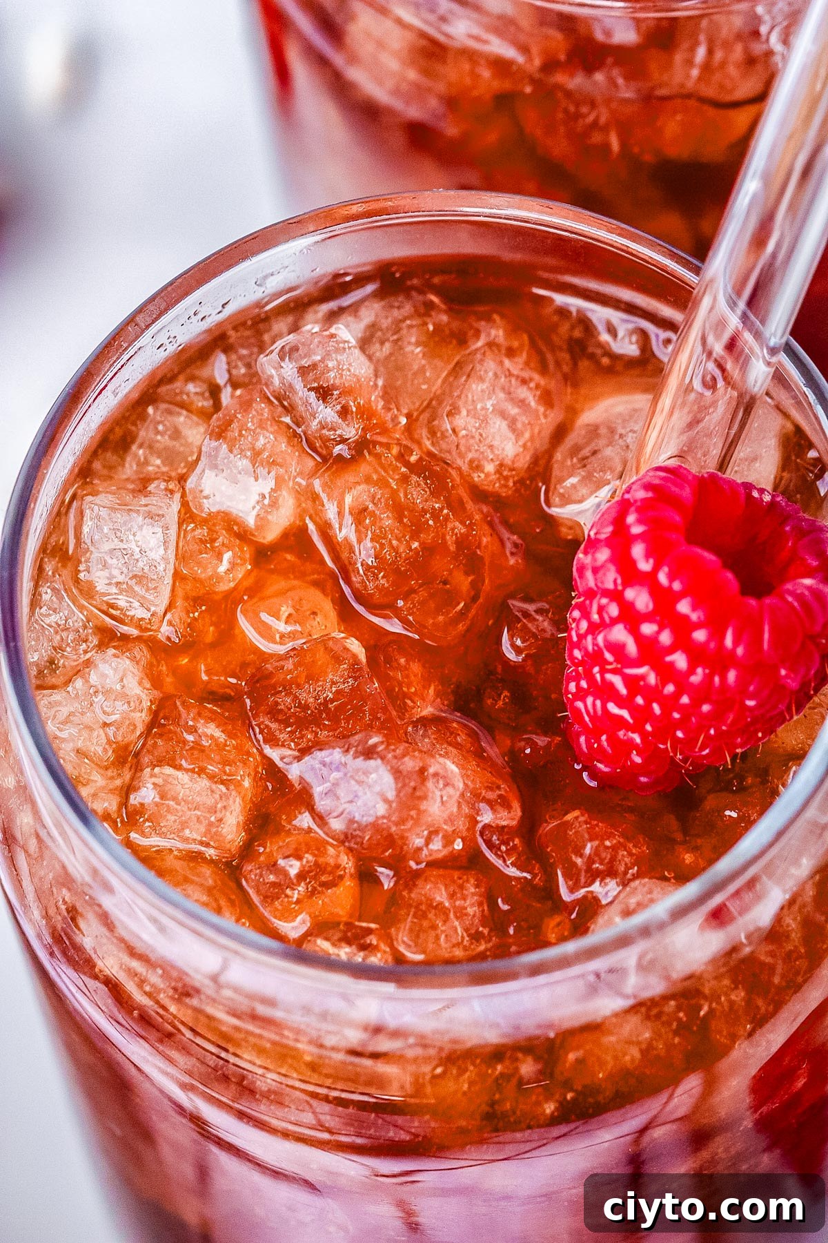 A Raspberry Dream in a glass with pebble ice, a raspberry, and a straw.