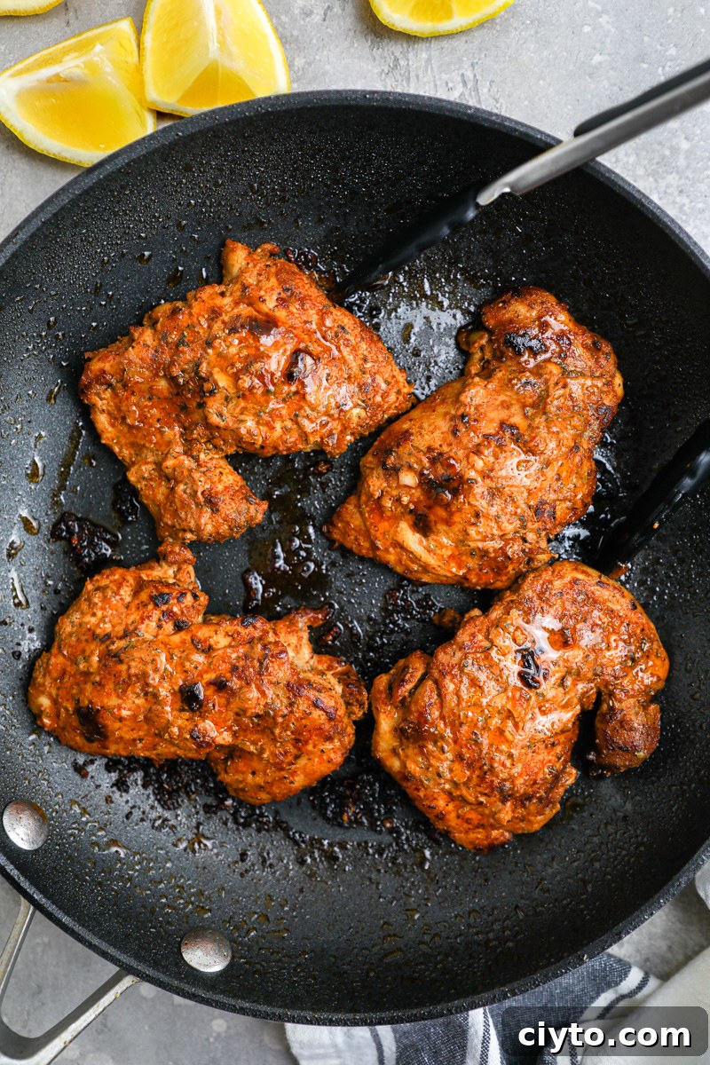 A large skillet filled with marinated chicken thighs sitting next to lemon wedges