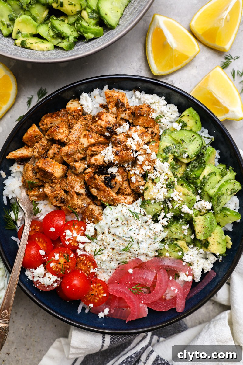 A large blue bowl filled with white rice, pickled onion, tomato, marinated chicken, homemade tzatziki and cucumber-avocado salad