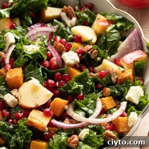 Kale and butternut squash salad with apple and pomegranate seeds in a large bowl.