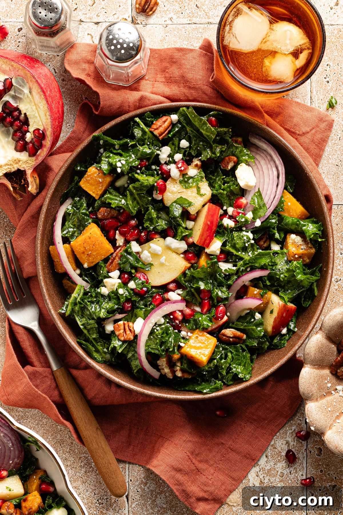 Kale and Butternut Squash Salad with Pomegranate and Apple 9 Kale butternut squash and pomegranate salad in a bowl on a table with a drink and a rust colored linen.