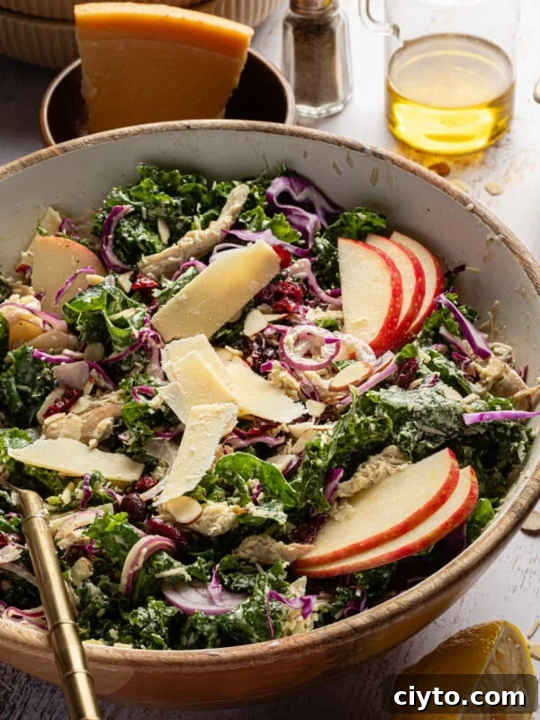 Kale chicken salad with sliced apples, parmesan cheese and a creamy dressing in a bowl.
