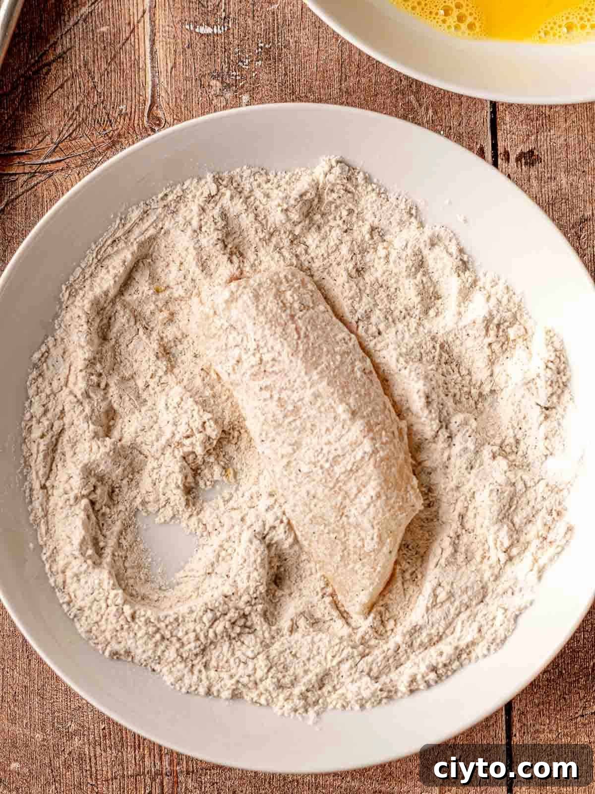 Piece of cod dipped into a bowl of flour.