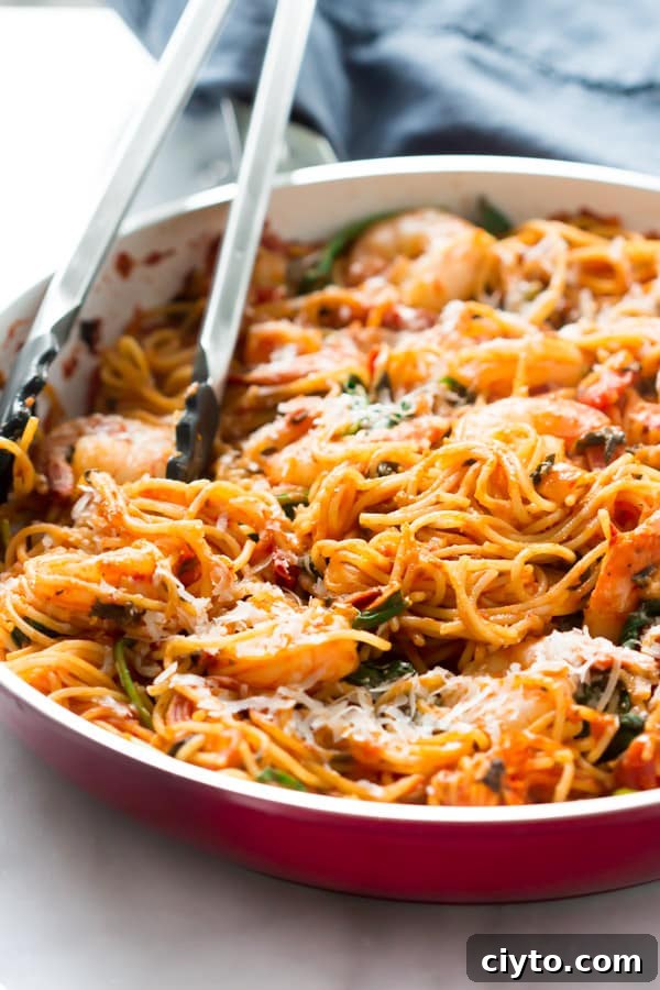 Shrimp pasta in a skillet with tongs inside.