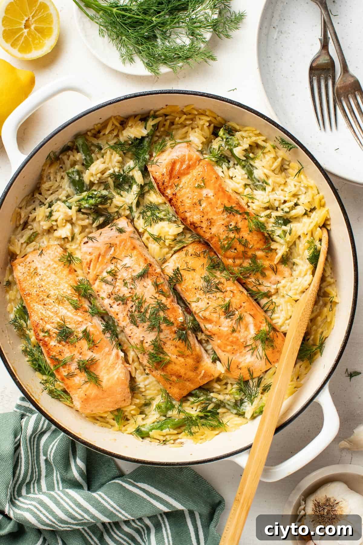 Seared salmon fillets in a cast iron pan with orzo and fresh herbs on top.