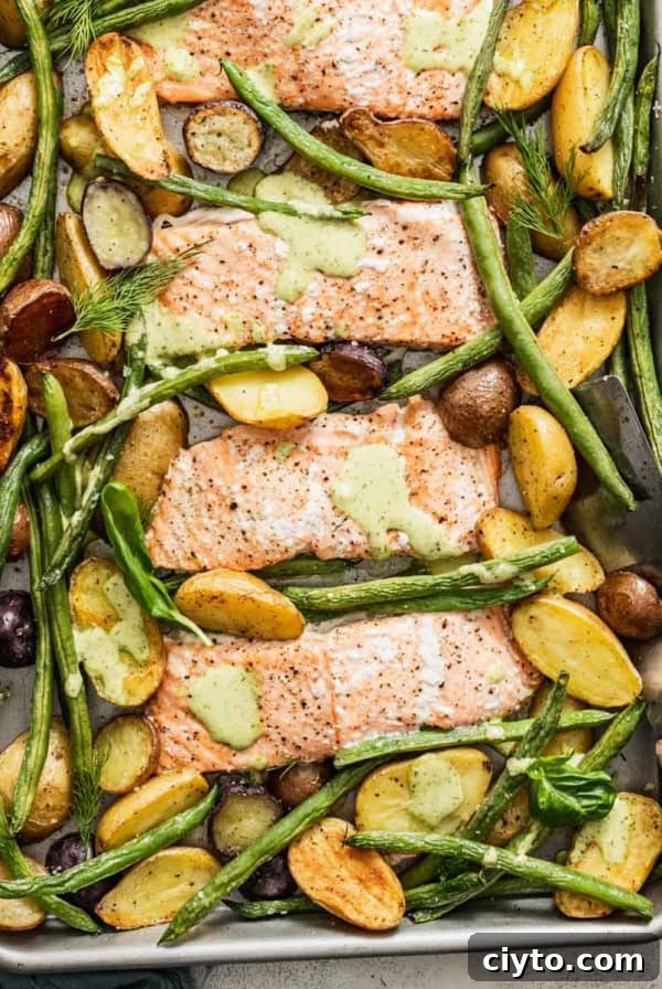 A sheet pan with baked salmon, an herb sauce, green beans and potatoes.