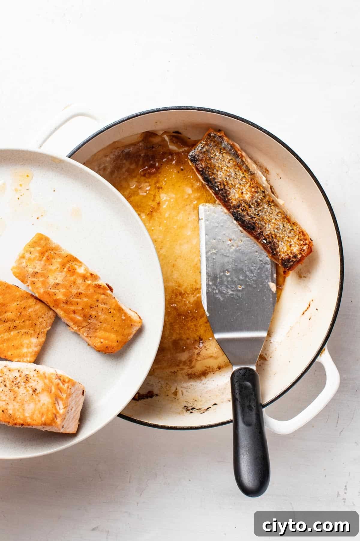 Salmon fillets being removed from a pan, golden brown after cooking.