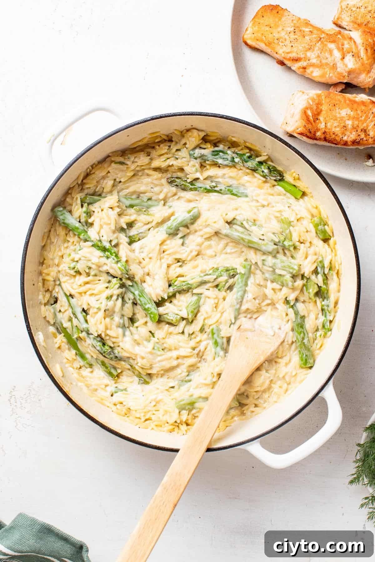 Adding in the creamy Boursin cheese and lemon to the cooked orzo in a large white pan.