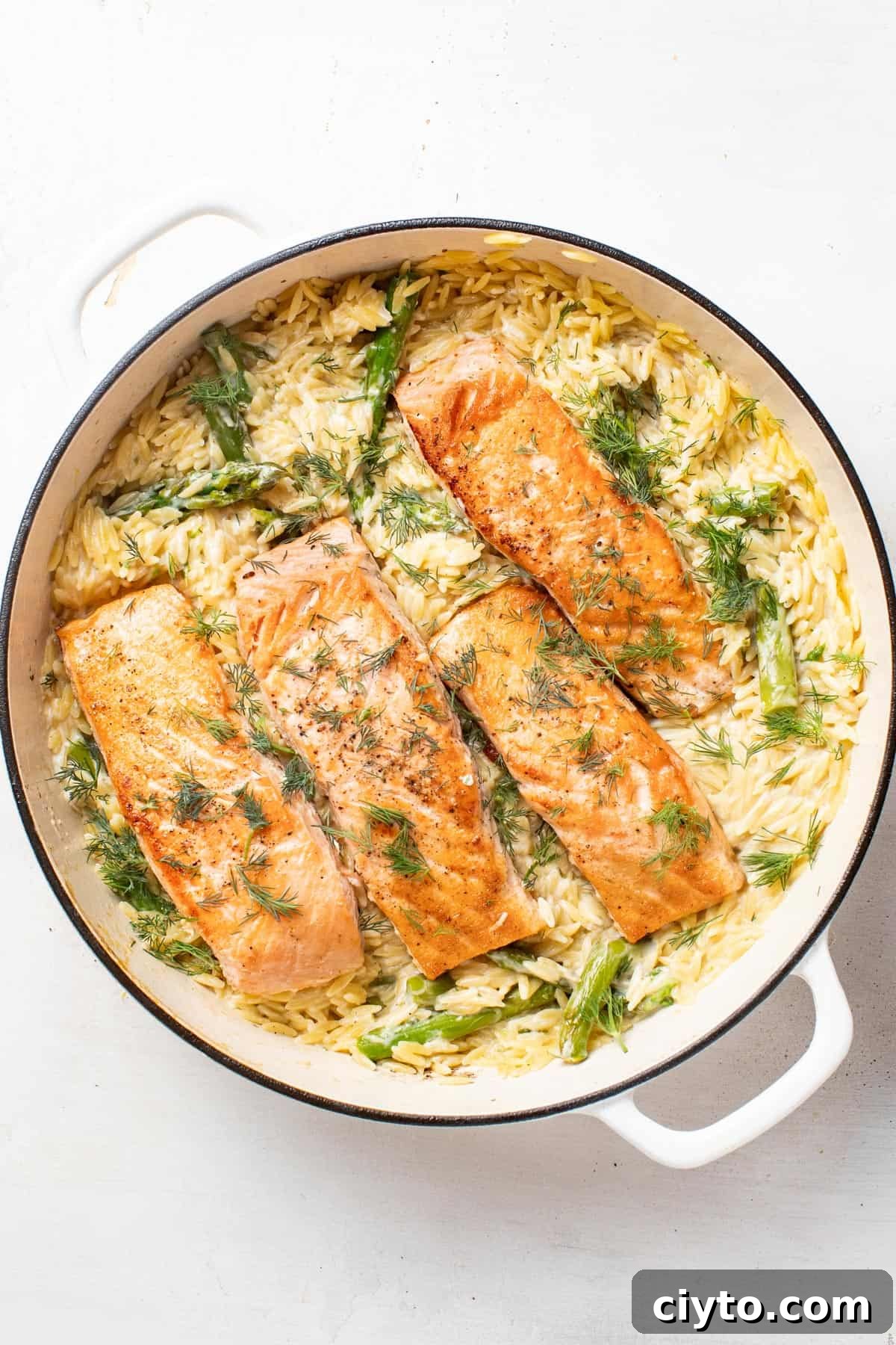 Salmon fillets nestled into the creamy asparagus and lemon orzo in the white pan.