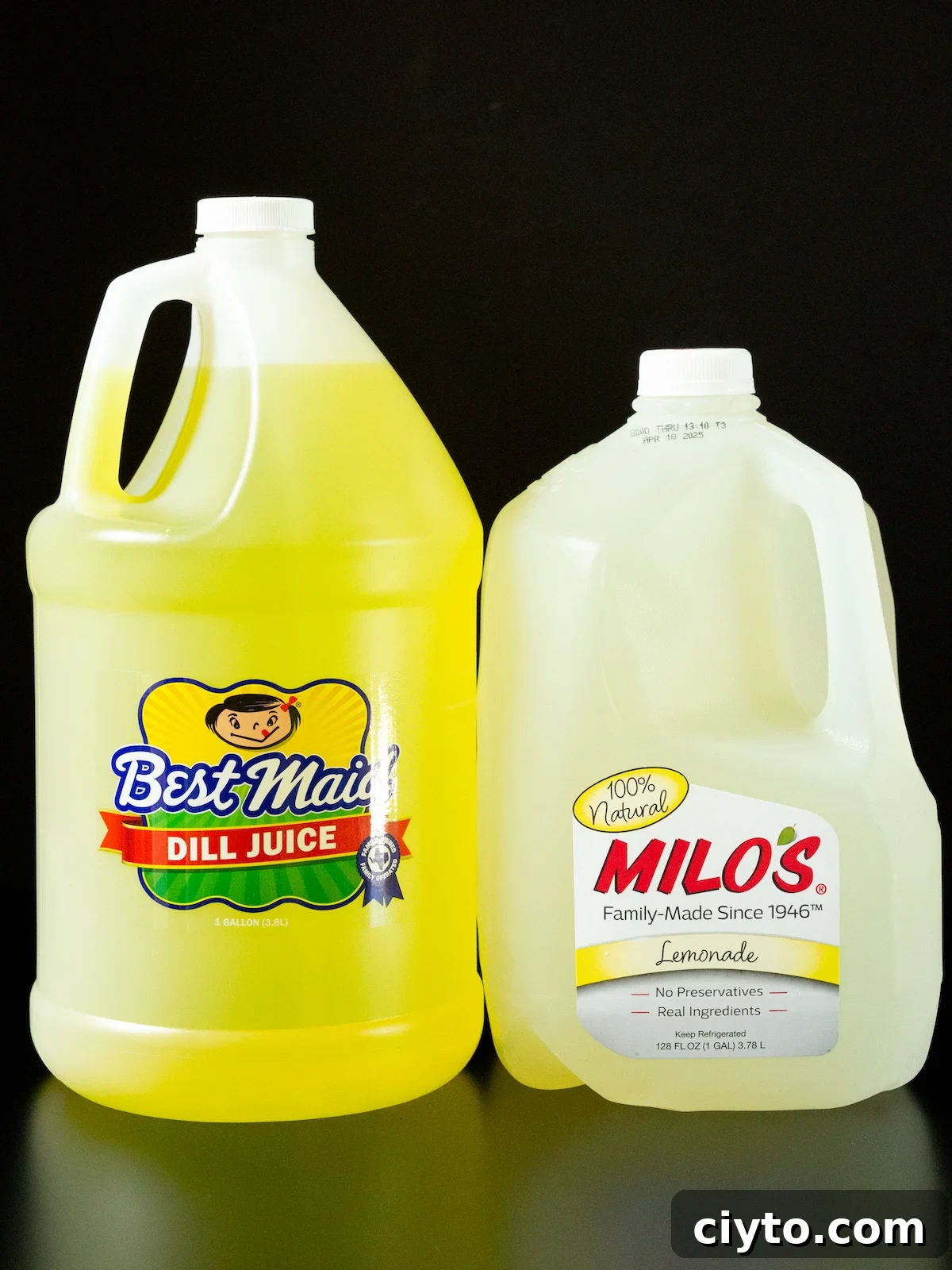 A gallon of dill pickle juice and a gallon jug of Milo's lemonade on a black background.