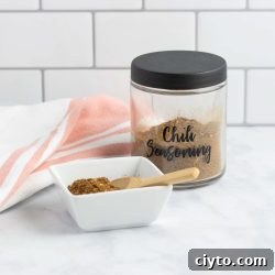 A jar of homemade chili seasoning beside a dish of the seasoning with a small wooden spoon.