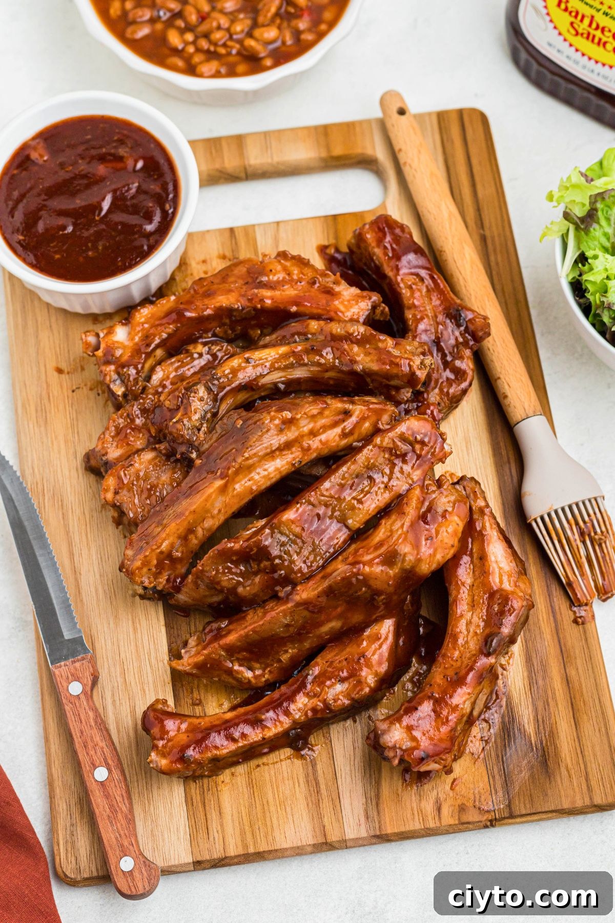 Juicy ribs cut individually, on a wooden cutting board with a steak knife and brush next to them.