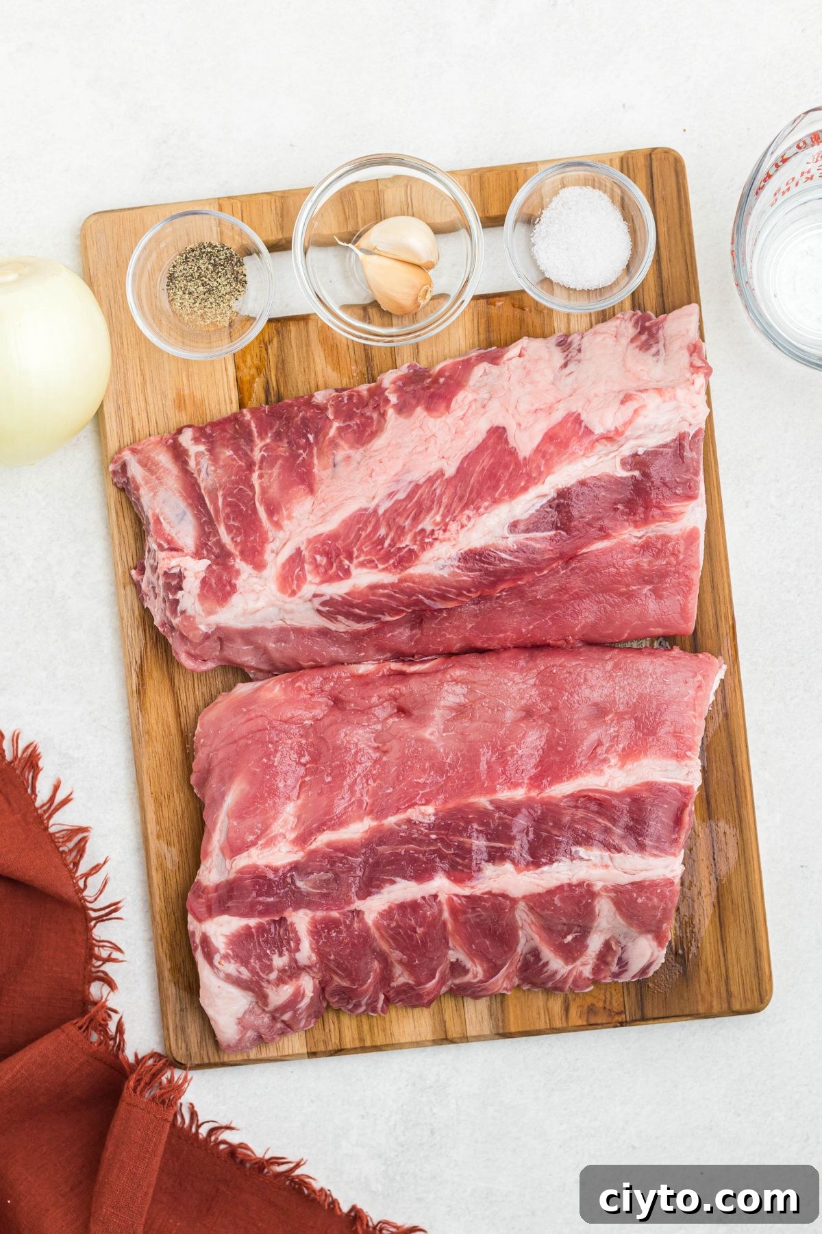 Uncooked ribs on a cutting board with seasonings in small bowls.