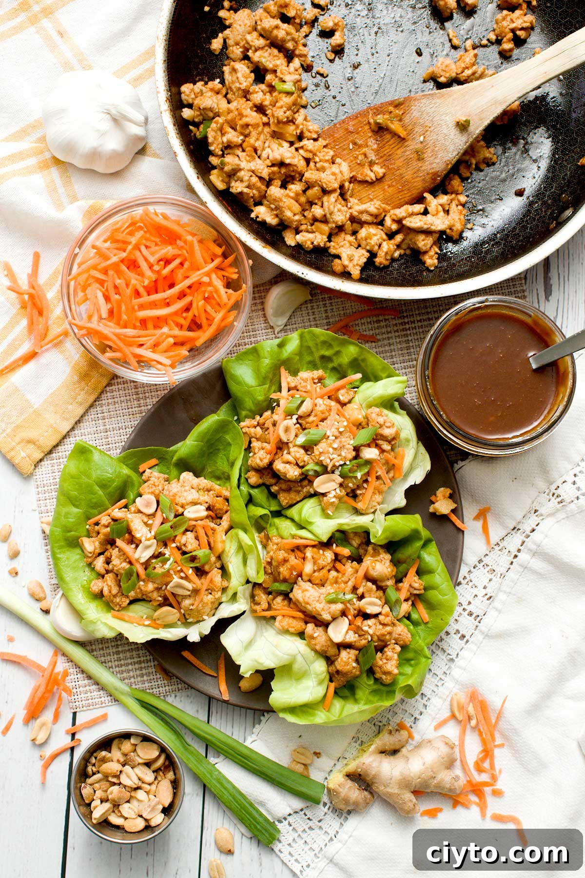 Three asian lettuce wraps with ground chicken and hoisin peanut sauce next to a skillet.