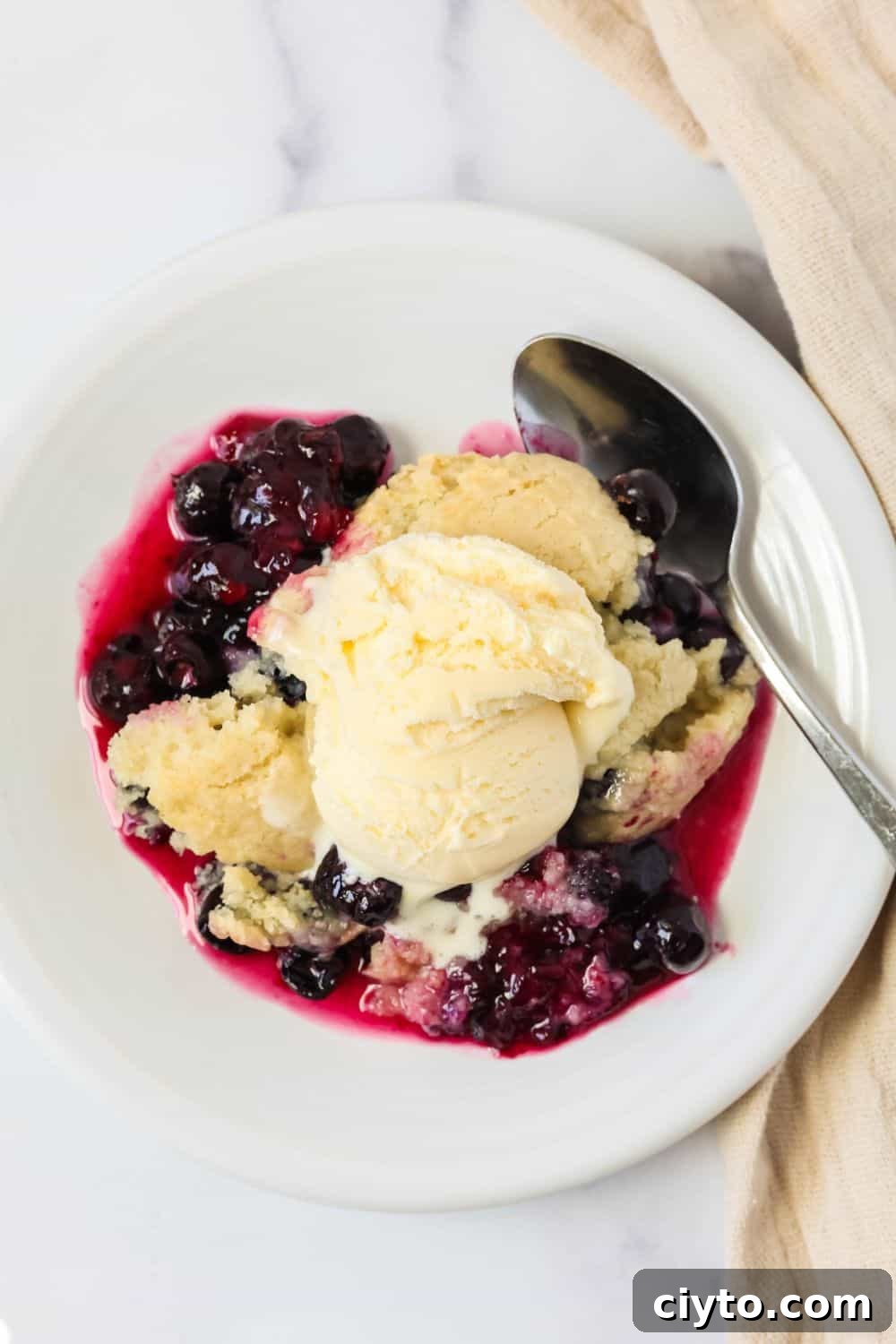 Quick Bisquick Blueberry Cobbler Recipe for Summer 5 Overhead view of a plate of Bisquick fresh blueberry cobbler topped with vanilla ice cream. A spoon is next to the cobbler.